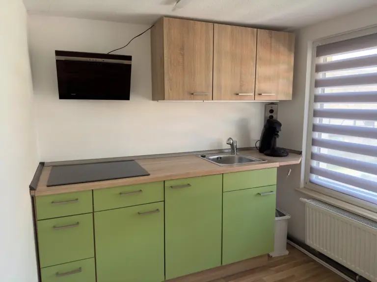 Kleine Küche im Obergeschoss mit grünen Schränken, Kochfeld, Spüle und Kaffeemaschine bei Monteurzimmer Jena.